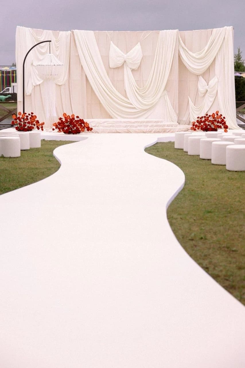 Outdoor ceremony with a draped backdrop and a long white aisle lined with florals